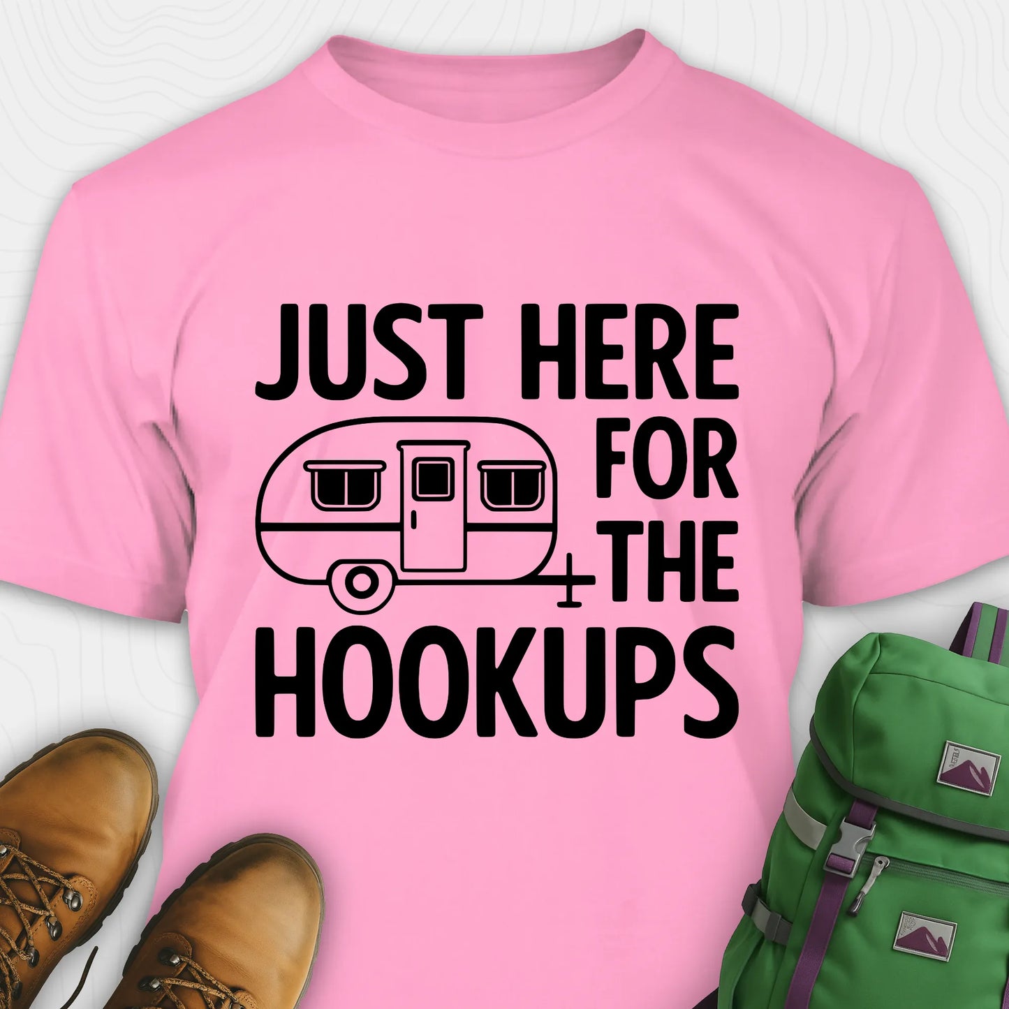 Pink hook ups t-shirt with trailer graphic and funny camping quote, paired with brown boots and a green backpack on a white background.