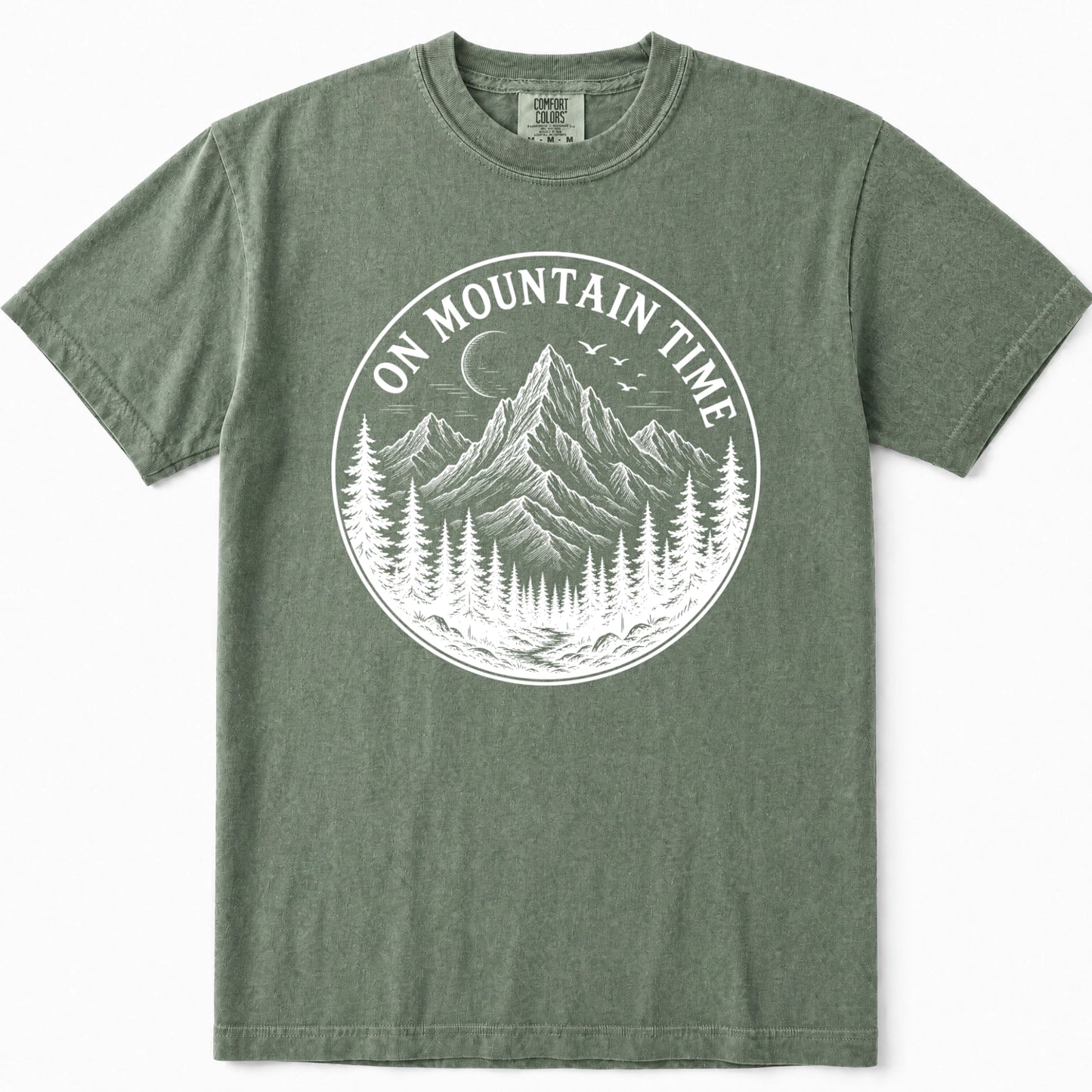 Moss green crewneck t-shirt featuring a large white circular graphic on the chest with a mountain, pine trees, and the text 'ON MOUNTAIN TIME'.