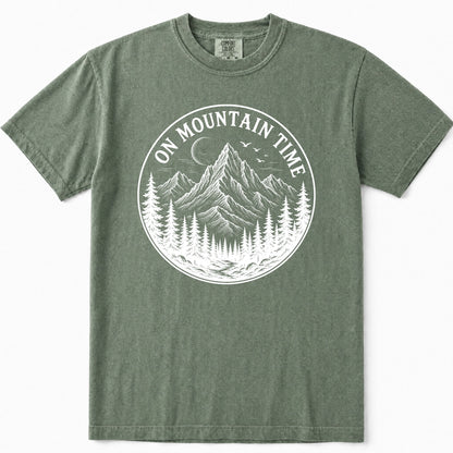 Moss green crewneck t-shirt featuring a large white circular graphic on the chest with a mountain, pine trees, and the text 'ON MOUNTAIN TIME'.