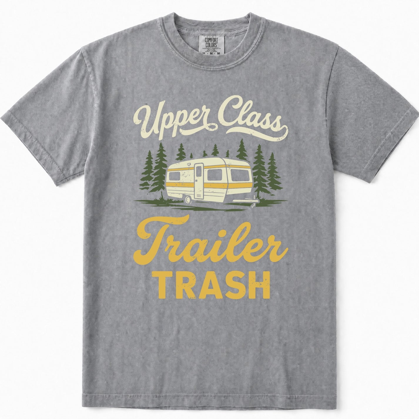 Grey short-sleeve t-shirt with a vintage-style graphic print that reads 'Upper Class Trailer TRASH' in cream and yellow lettering, featuring an illustration of a cream and yellow camper trailer surrounded by green pine trees.