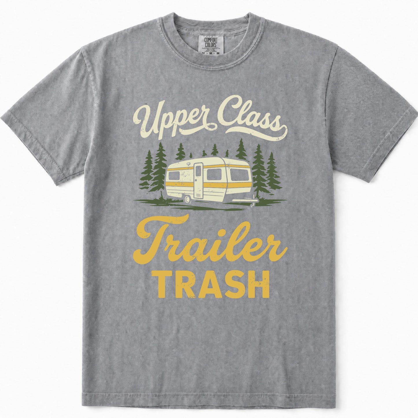 Grey short-sleeve t-shirt with a vintage-style graphic print that reads 'Upper Class Trailer TRASH' in cream and yellow lettering, featuring an illustration of a cream and yellow camper trailer surrounded by green pine trees.