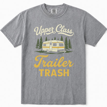 Grey short-sleeve t-shirt with a vintage-style graphic print that reads 'Upper Class Trailer TRASH' in cream and yellow lettering, featuring an illustration of a cream and yellow camper trailer surrounded by green pine trees.