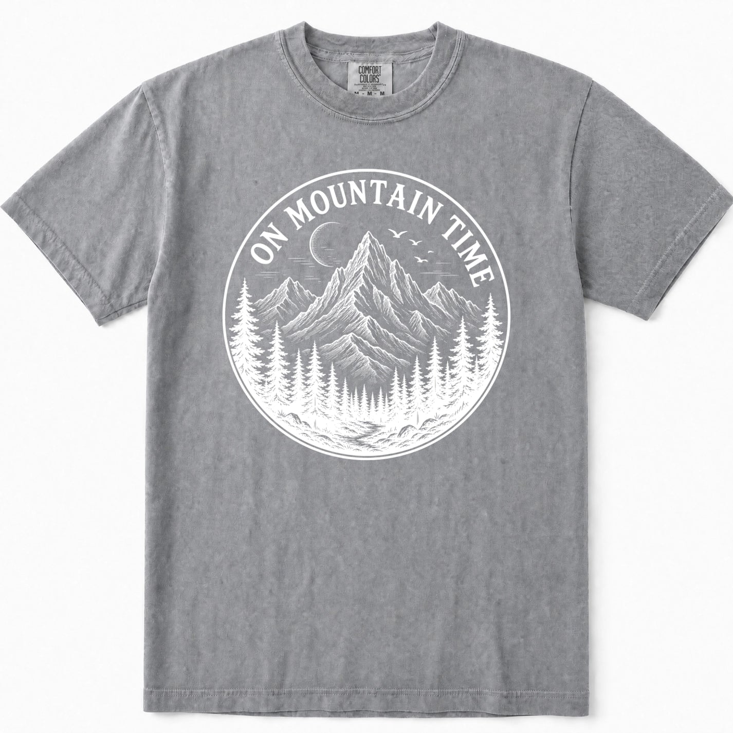 Grey crewneck t-shirt featuring a white circular graphic print on the front with a mountain, pine trees, birds, and the text 'ON MOUNTAIN TIME'.