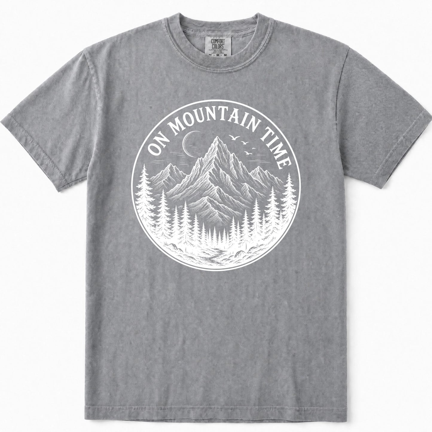 Grey crewneck t-shirt featuring a white circular graphic print on the front with a mountain, pine trees, birds, and the text 'ON MOUNTAIN TIME'.
