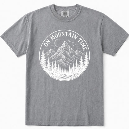 Grey crewneck t-shirt featuring a white circular graphic print on the front with a mountain, pine trees, birds, and the text 'ON MOUNTAIN TIME'.
