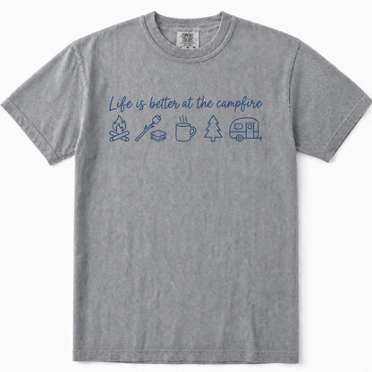 Grey short-sleeve crewneck t-shirt featuring a blue graphic print on the front with the text 'Life is better at the campfire' and simple icons for a campfire, marshmallow, mug, pine tree, and camper trailer.