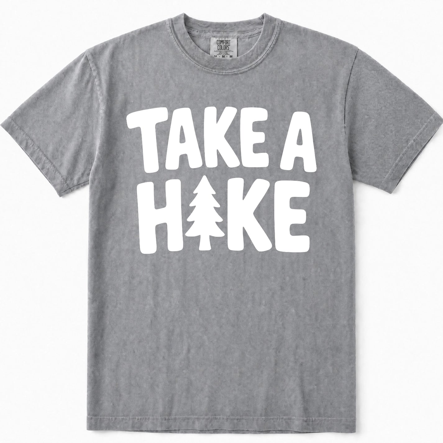 Grey short-sleeve crewneck t-shirt with a bold white graphic print on the front that reads 'TAKE A HAKE' with a pine tree icon replacing the letter 'I'.