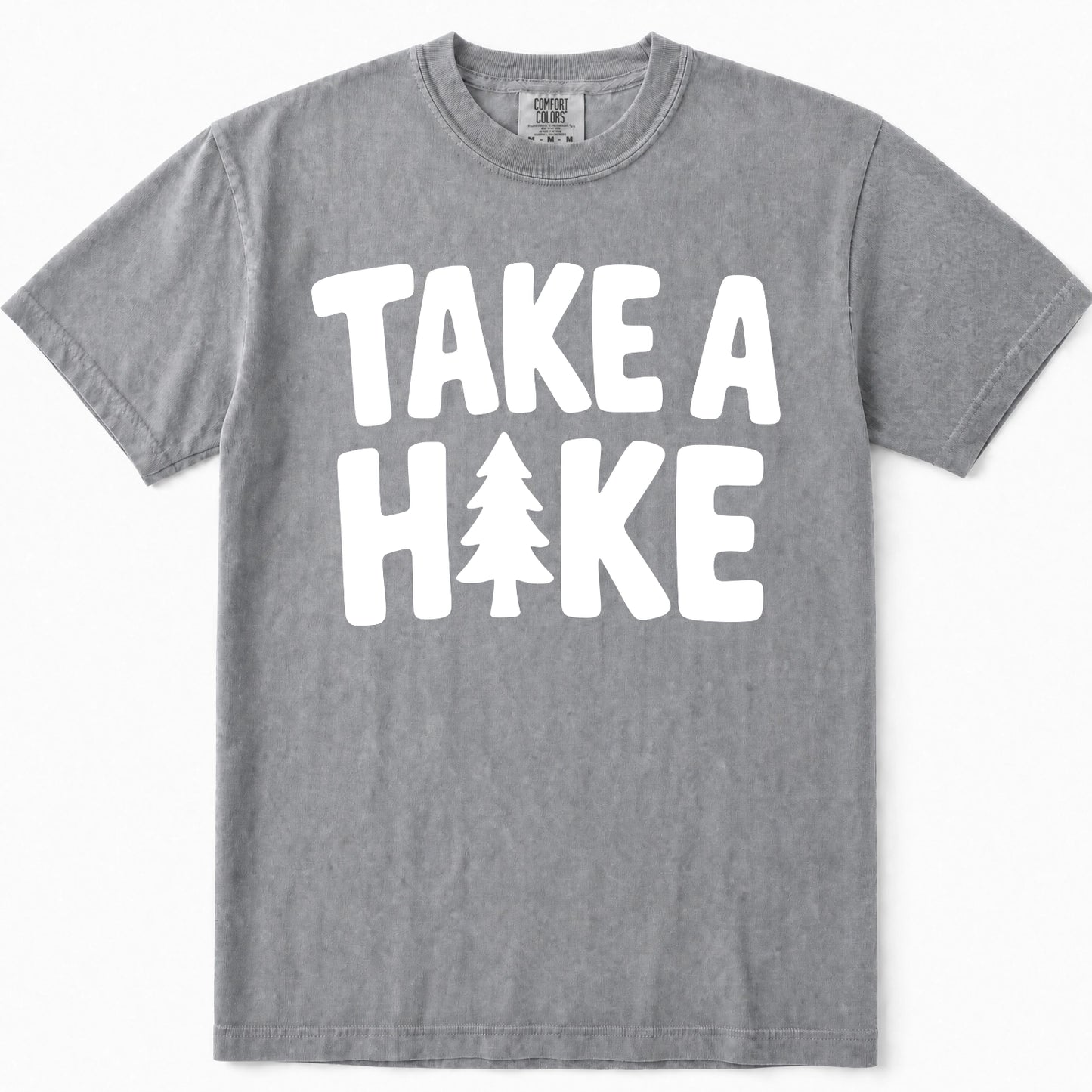 Grey short-sleeve crewneck t-shirt with a bold white graphic print on the front that reads 'TAKE A HAKE' with a pine tree icon replacing the letter 'I'.