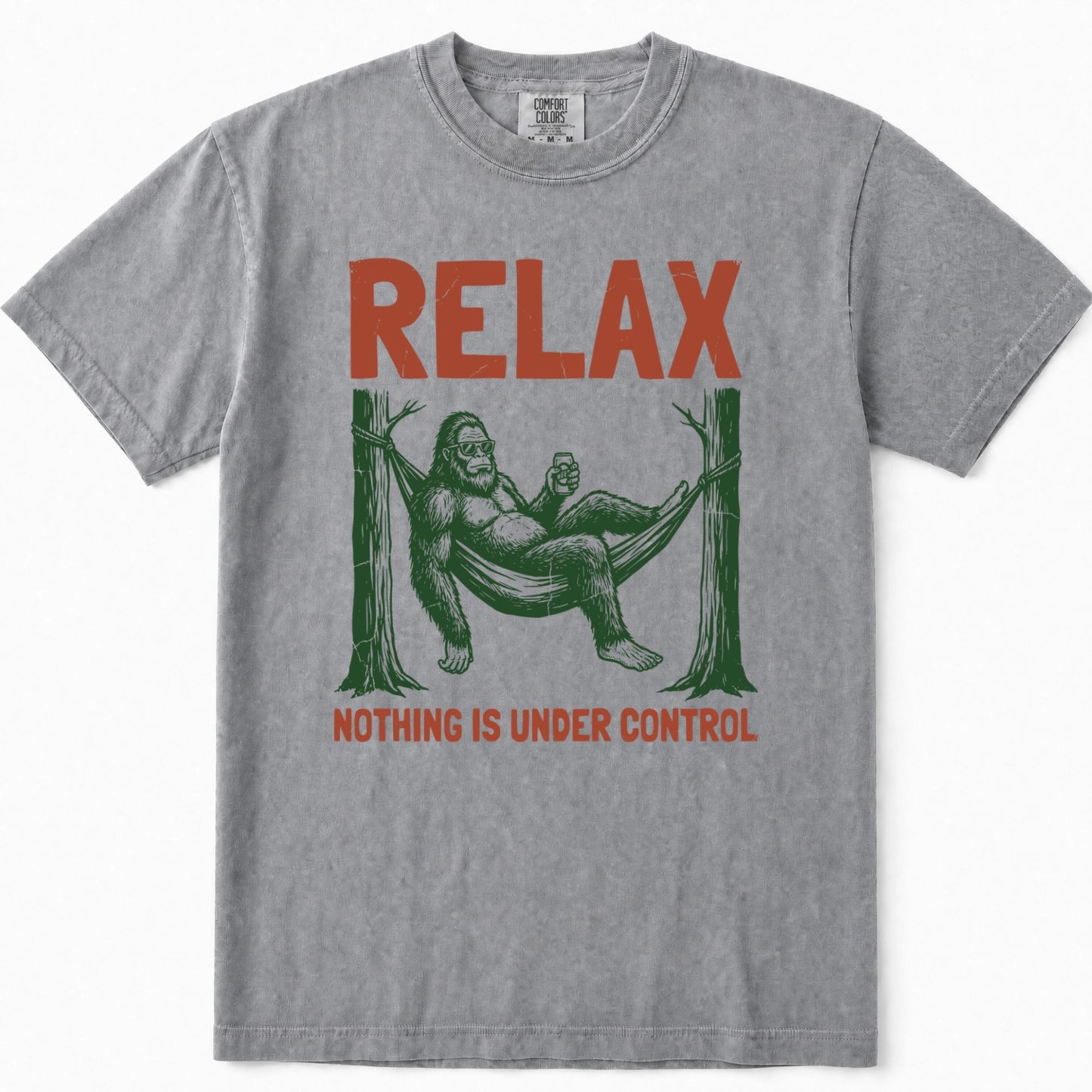 Grey crewneck t-shirt featuring a vintage-style graphic of Bigfoot lounging in a hammock with the text 'RELAX' above and 'NOTHING IS UNDER CONTROL' below in red.