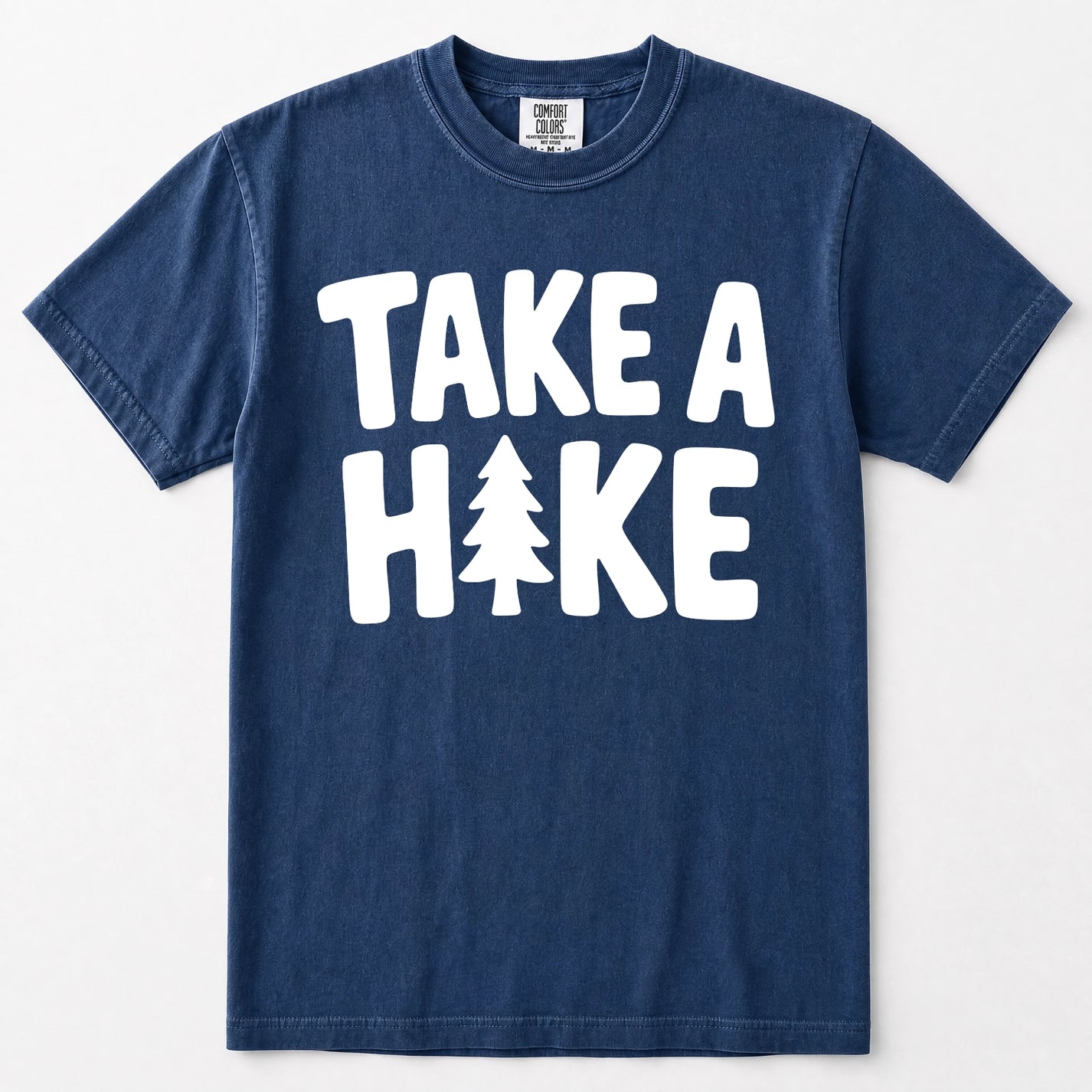 Navy blue short-sleeve t-shirt with a bold white graphic print reading 'TAKE A HAKE' across the chest, where the letter 'I' is replaced by a small pine tree. The shirt is displayed flat against a clean, light off-white background.
