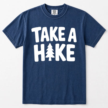 Navy blue short-sleeve t-shirt with a bold white graphic print reading 'TAKE A HAKE' across the chest, where the letter 'I' is replaced by a small pine tree. The shirt is displayed flat against a clean, light off-white background.