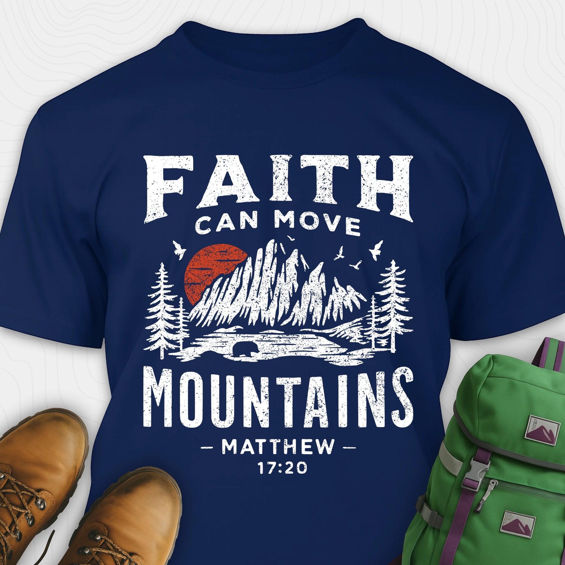 Navy bible verse t-shirt with 'Faith can move mountains' design and hiking boots and backpack on a white background