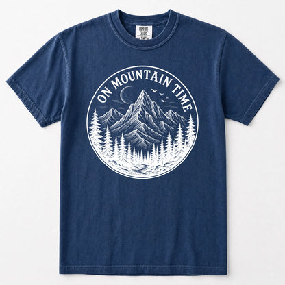 Navy blue short-sleeve t-shirt with a white circular graphic on the chest depicting a mountain, pine trees, birds, and a crescent moon, with the text 'ON MOUNTAIN TIME'.