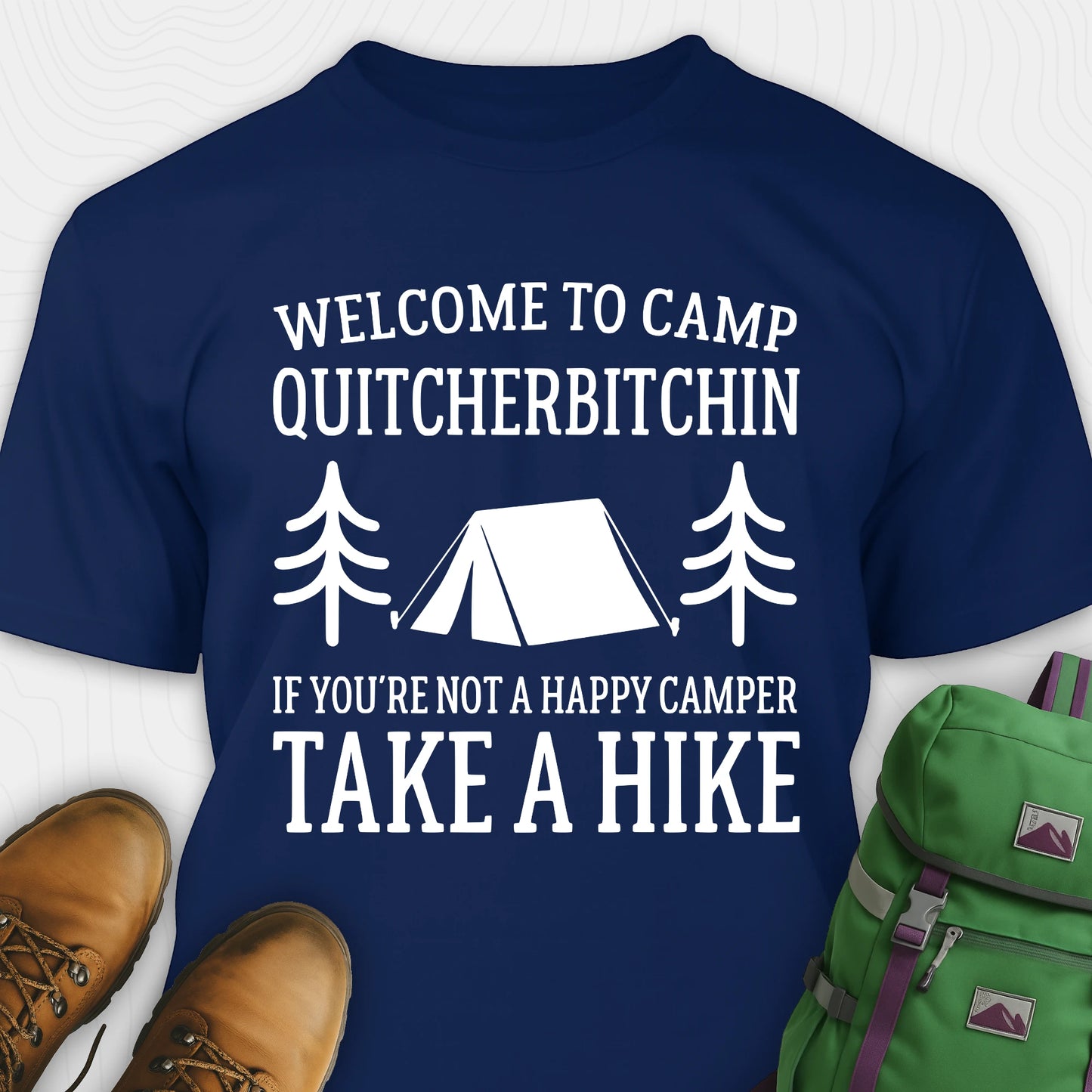 Navy Camp Quit Your Bitchin T-Shirt with humorous camping text design, paired with hiking boots and a green backpack on a white background.