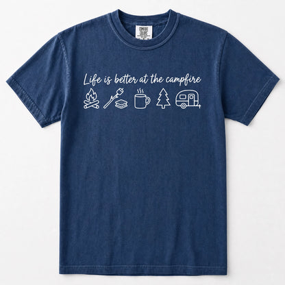 Navy blue short-sleeve crewneck t-shirt with a white graphic print on the chest that reads 'Life is better at the campfire' above simple line drawings of a campfire, roasting marshmallow, mug, pine tree, and camper trailer.