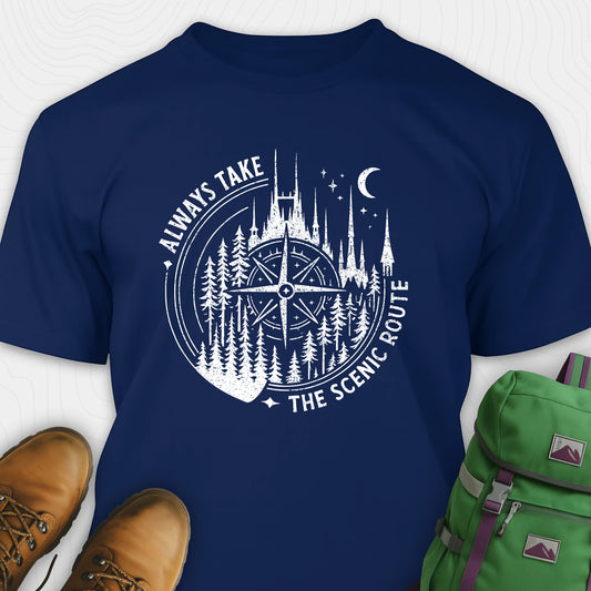 Navy blue Always Take The Scenic Route t-shirt with white compass design and nature design, paired with brown boots and a green backpack on a light grey background.