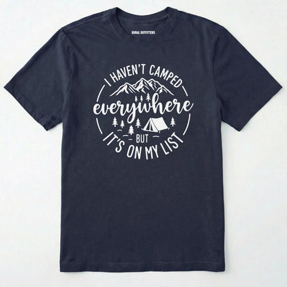 Navy funny camping shirt saying with mountains, trees, tent graphic and "I Haven't Camped Everywhere But It's On My List" text on a white background.