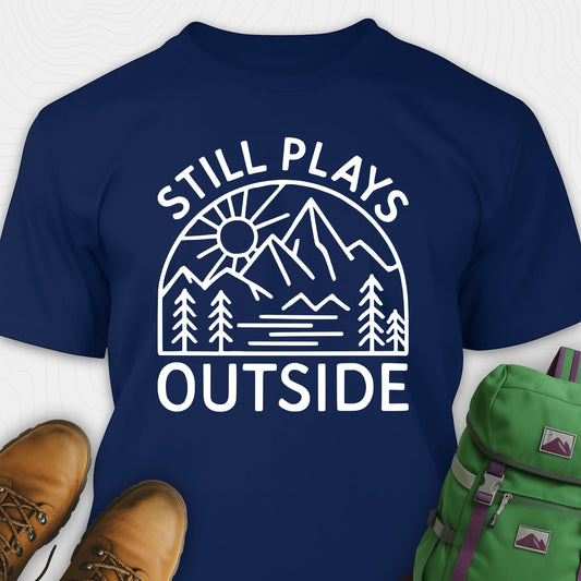 Navy blue t-shirt with 'Still Plays Outside' graphic design, paired with brown boots and a green backpack on a light gray background.