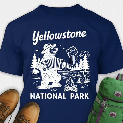 Navy t-shirt with a brown bear playing an accordion and “Yellowstone National Park” text, styled with hiking boots and a green backpack.