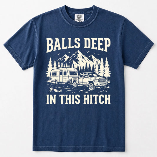 Navy blue short-sleeve crewneck t-shirt with a white graphic print on the front. The graphic features the text 'BALLS DEEP IN THIS HITCH' surrounding an illustration of a pickup truck towing a camper trailer with mountains and pine trees in the background.