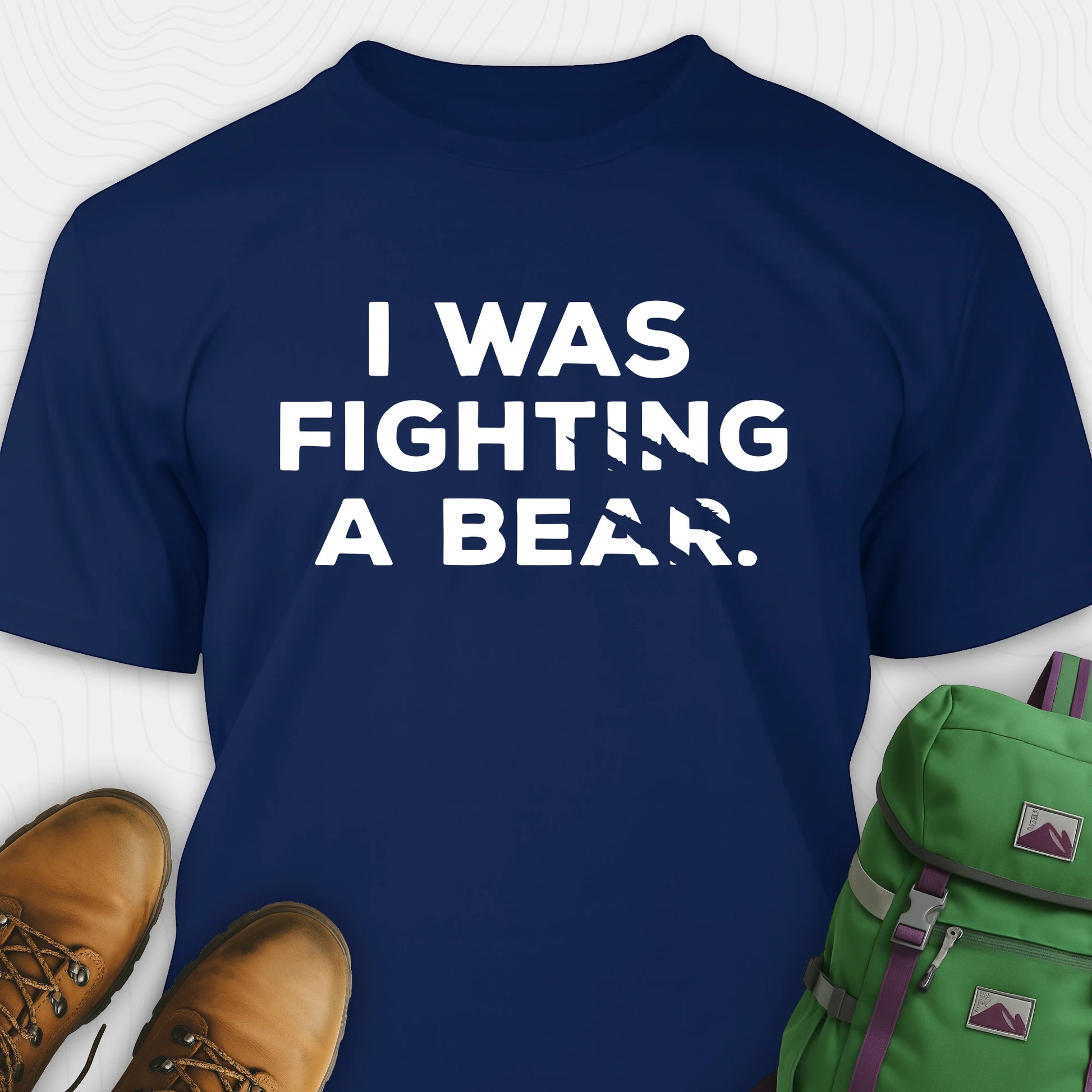 Navy I was fighting a bear shirt with a bear scratch mark graphic, paired with brown boots and a green backpack on a white background.