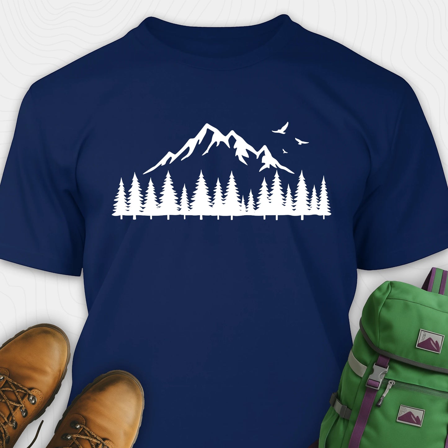 Navy wild t-shirt with a minimalist mountain and pine tree graphic, shown flat with boots and a backpack