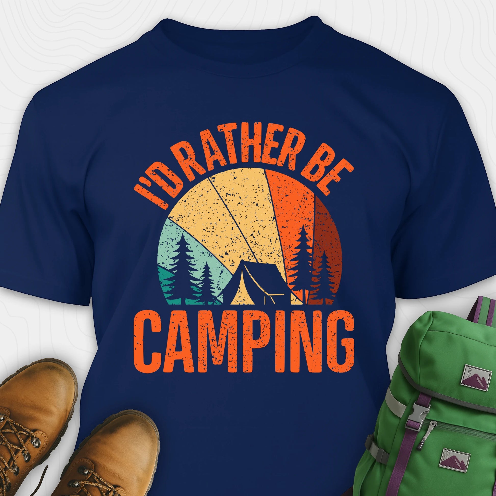 Navy blue t-shirt with 'I'd Rather Be Camping' graphic design, paired with brown boots and a green backpack on a white background.