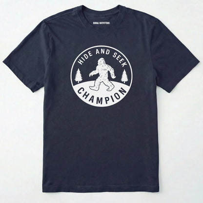 Navy bigfoot hide and seek champion shirt with forest emblem on a white background.