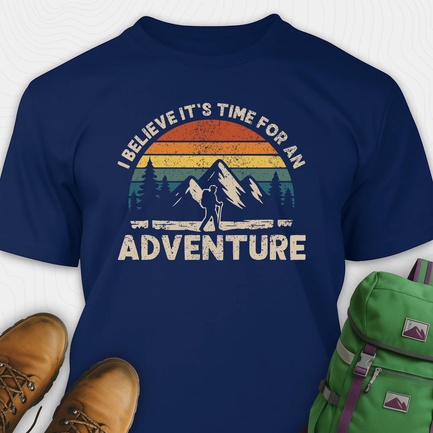 Navy backpacking shirt with mountain graphic and 'I believe it's time for an adventure' text, paired with brown boots and a green backpack.