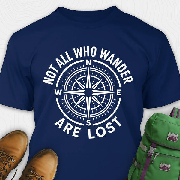 Navy blue Not All Who Wander Are Lost T-shirt with compass design and text, paired with brown shoes and a green backpack on a white background.