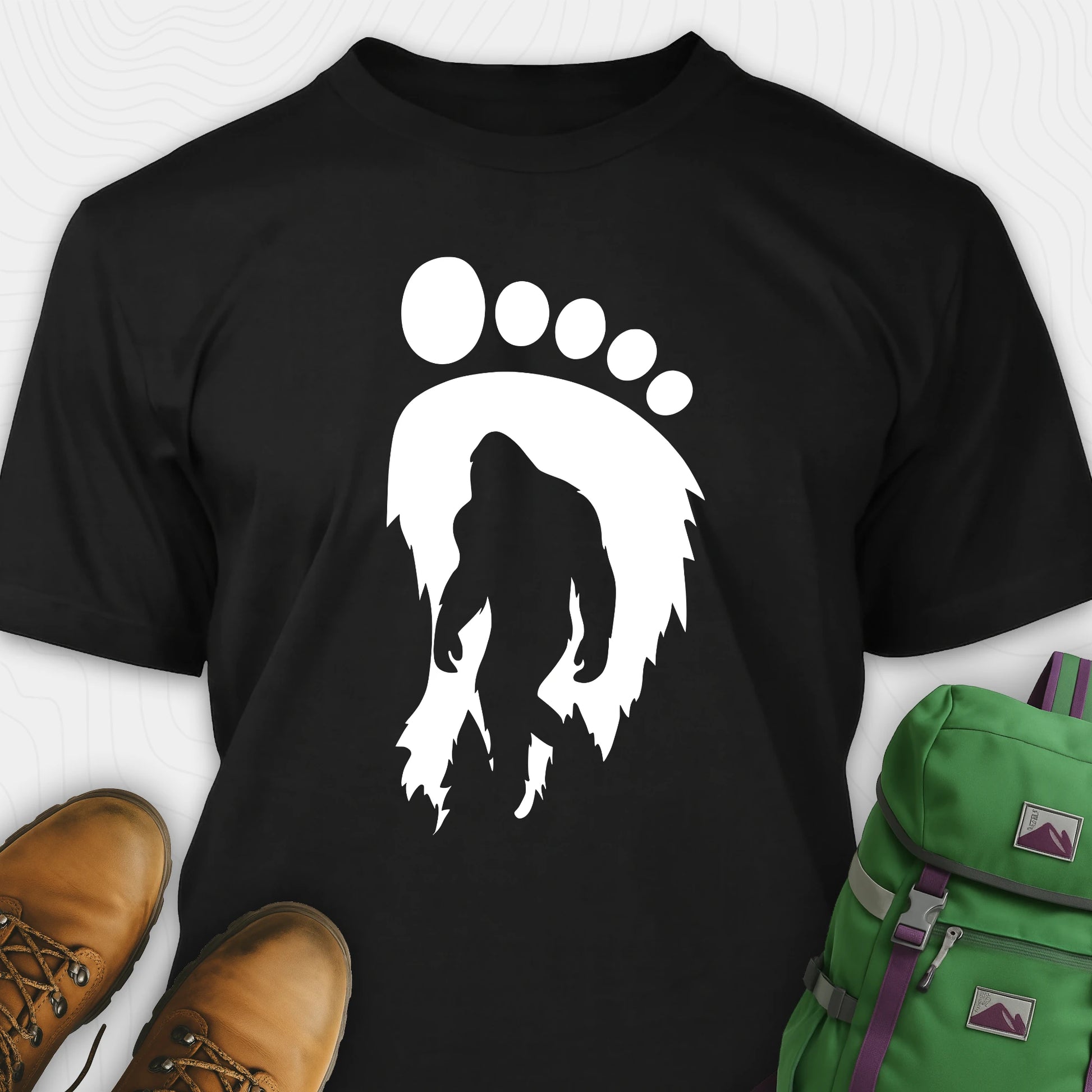 Black bigfoot t-shirt with cryptid themed footprint graphic and sasquatch silhouette