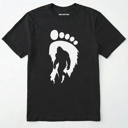 Black bigfoot t-shirt with cryptid-themed footprint graphic and sasquatch silhouette on a white background.