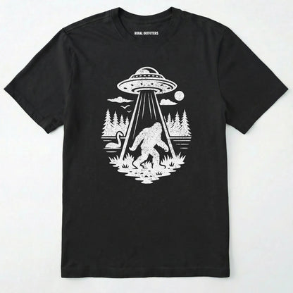 Black monster shirt with Bigfoot, a forest scene, and a UFO beam graphic on a white background.