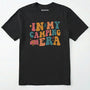 Black cute camping shirt with colorful retro ⊜in my camping era⊝ graphic on a white background.
