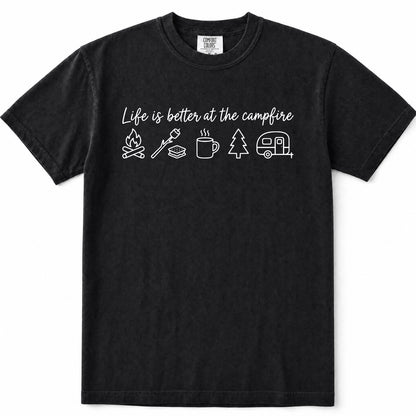 Black short-sleeve crewneck t-shirt with a white graphic print on the chest that reads 'Life is better at the campfire' above simple icons of a campfire, marshmallow, mug, pine tree, and camper trailer.