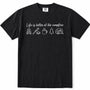 Black short-sleeve crewneck t-shirt with a white graphic print on the chest that reads 'Life is better at the campfire' above simple icons of a campfire, marshmallow, mug, pine tree, and camper trailer.