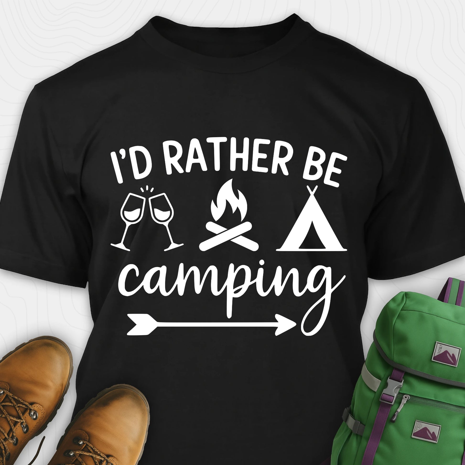 Black women's camping shirt with 'I'd Rather Be Camping' design, green backpack, and brown shoes on a white background