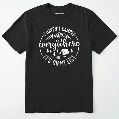 Black funny camping shirt saying with mountains, trees, tent graphic and "I Haven't Camped Everywhere But It's On My List" text on a white background.