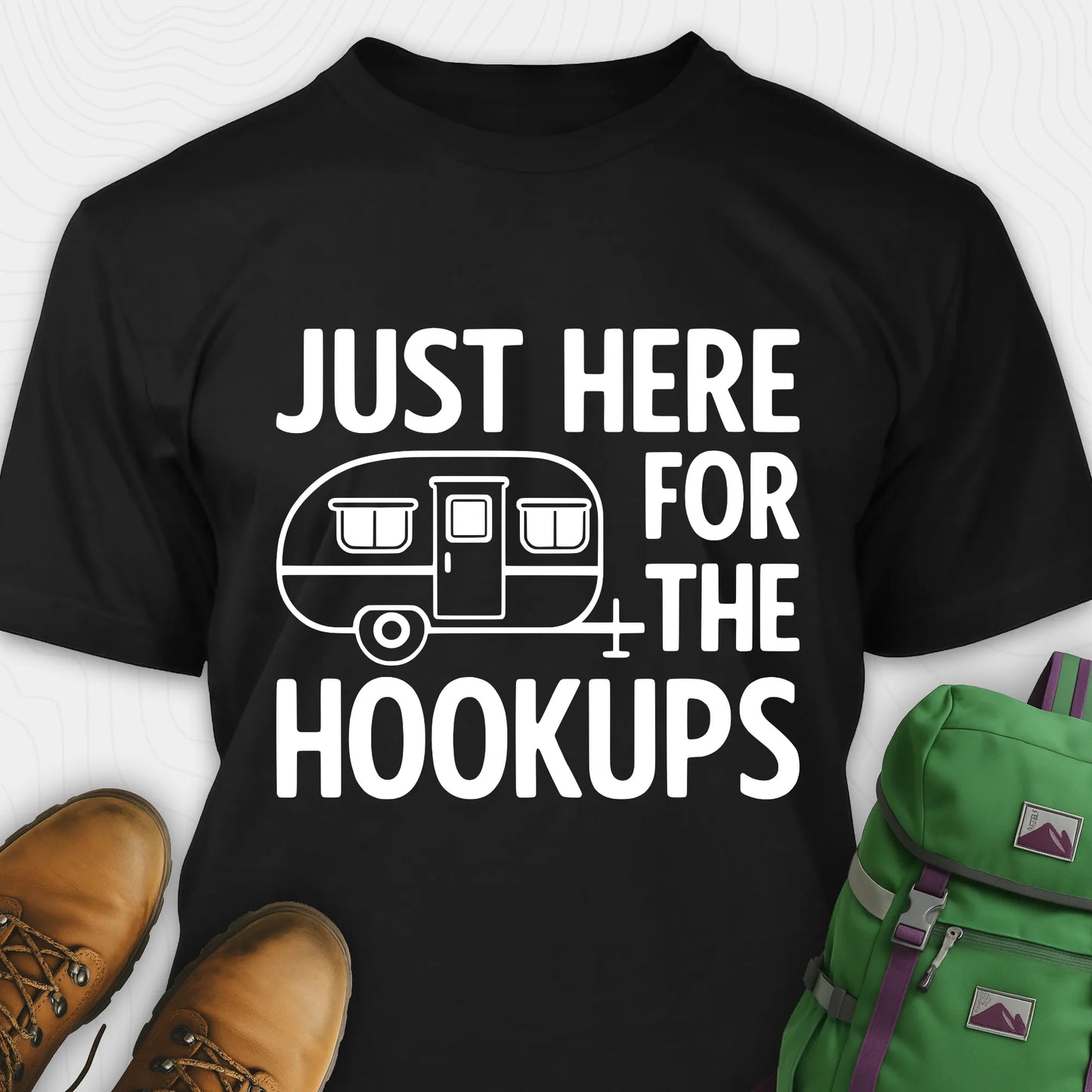 Black hook ups t-shirt with trailer graphic and funny camping quote, paired with brown boots and a green backpack on a white background.