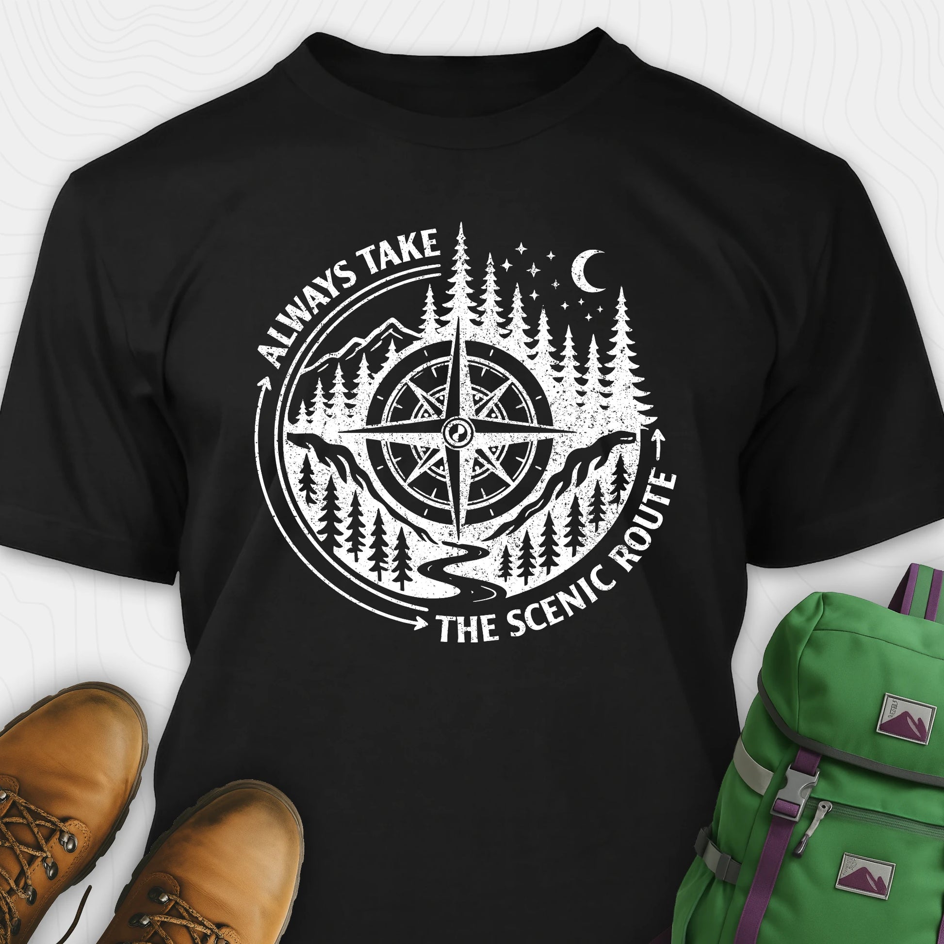 Black always take the scenic route t-shirt with compass graphic and text, paired with hiking boots and a green backpack.