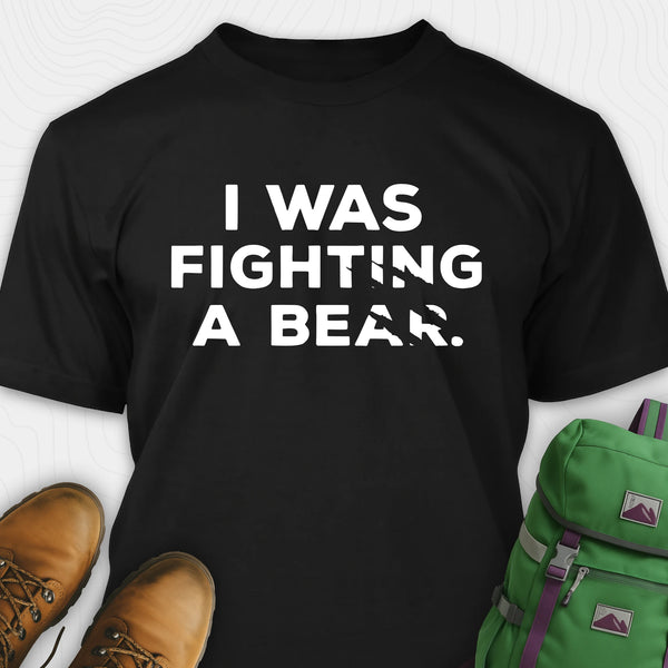 Black I was fighting a bear shirt with a bear scratch mark graphic, paired with brown boots and a green backpack on a white background.