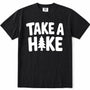 Black short-sleeve crewneck t-shirt with a white graphic print on the front that reads 'TAKE A HAKE' with a pine tree icon representing the letter 'I'.