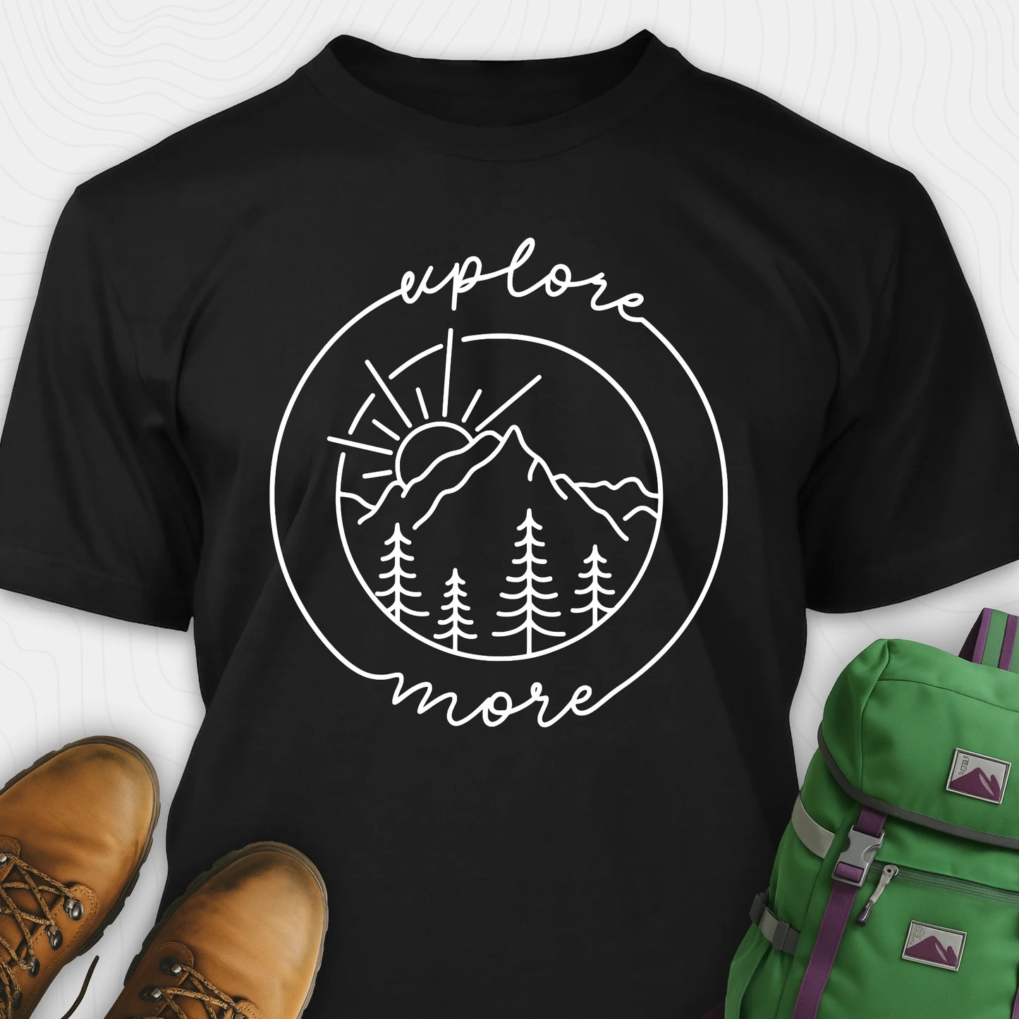 Black explorer shirt with 'explore more' graphic design, brown boots, and green backpack on a white background