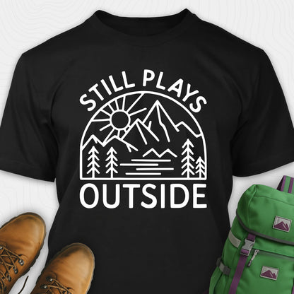 Black t-shirt with 'Still Plays Outside' graphic design, paired with brown boots and a green backpack on a light gray background.