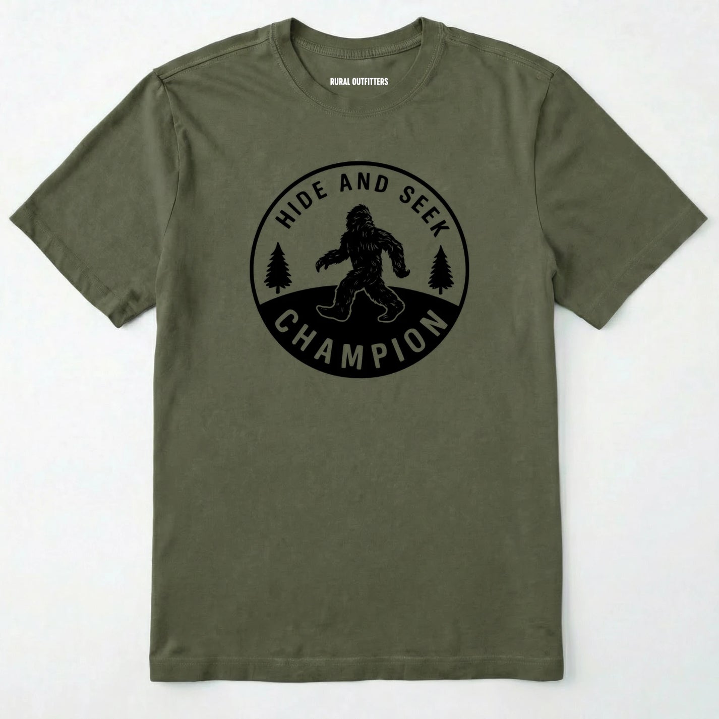 Military Green bigfoot hide and seek champion shirt with forest emblem on a white background.