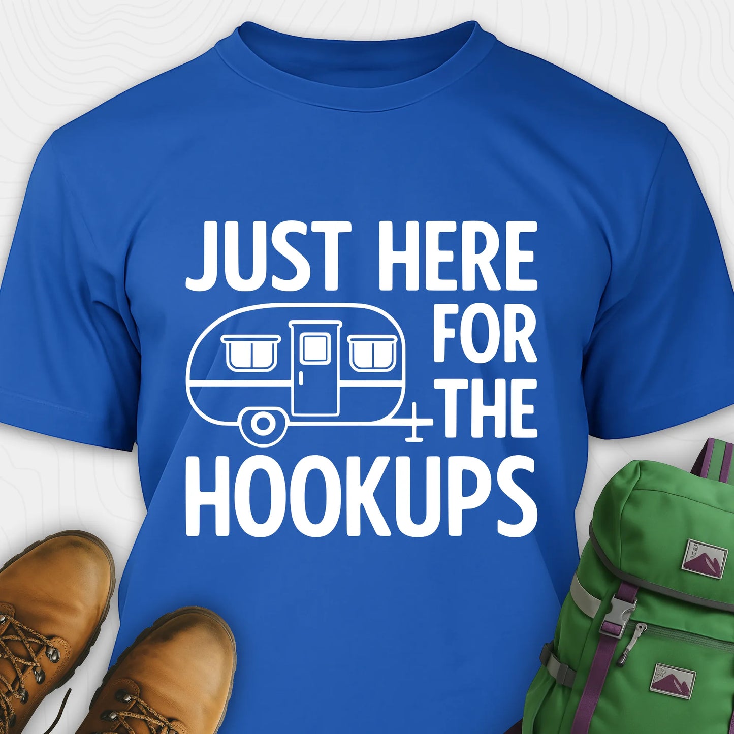 Blue hook ups t-shirt with trailer graphic and funny camping quote, paired with brown boots and a green backpack on a white background.