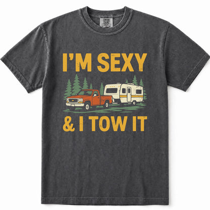 Pepper heathered t-shirt with a graphic print that reads 'I'M SEXY & I TOW IT' in yellow text, featuring an illustration of an orange pickup truck towing a cream camper trailer with green pine trees in the background.