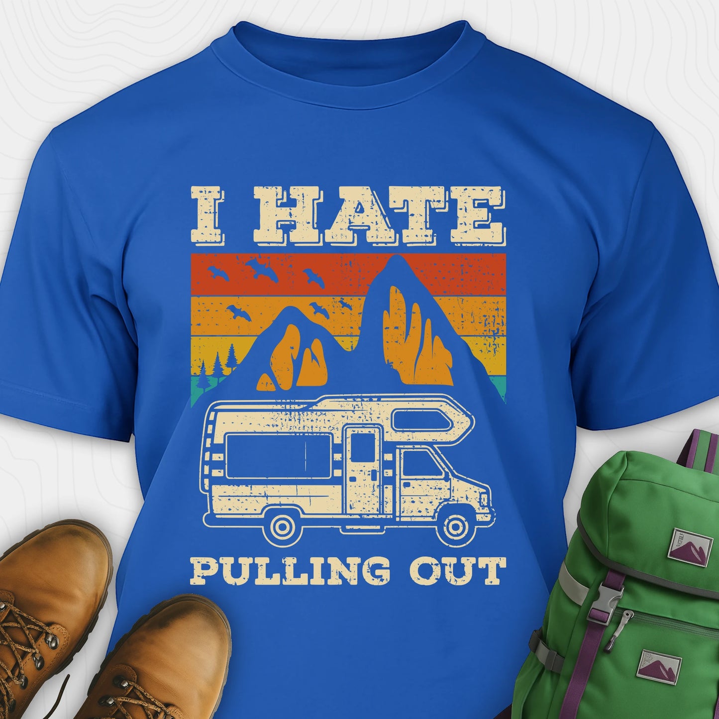 Blue I hate pulling out shirt with a graphic design of an RV and mountains, displayed with brown boots and a green backpack.