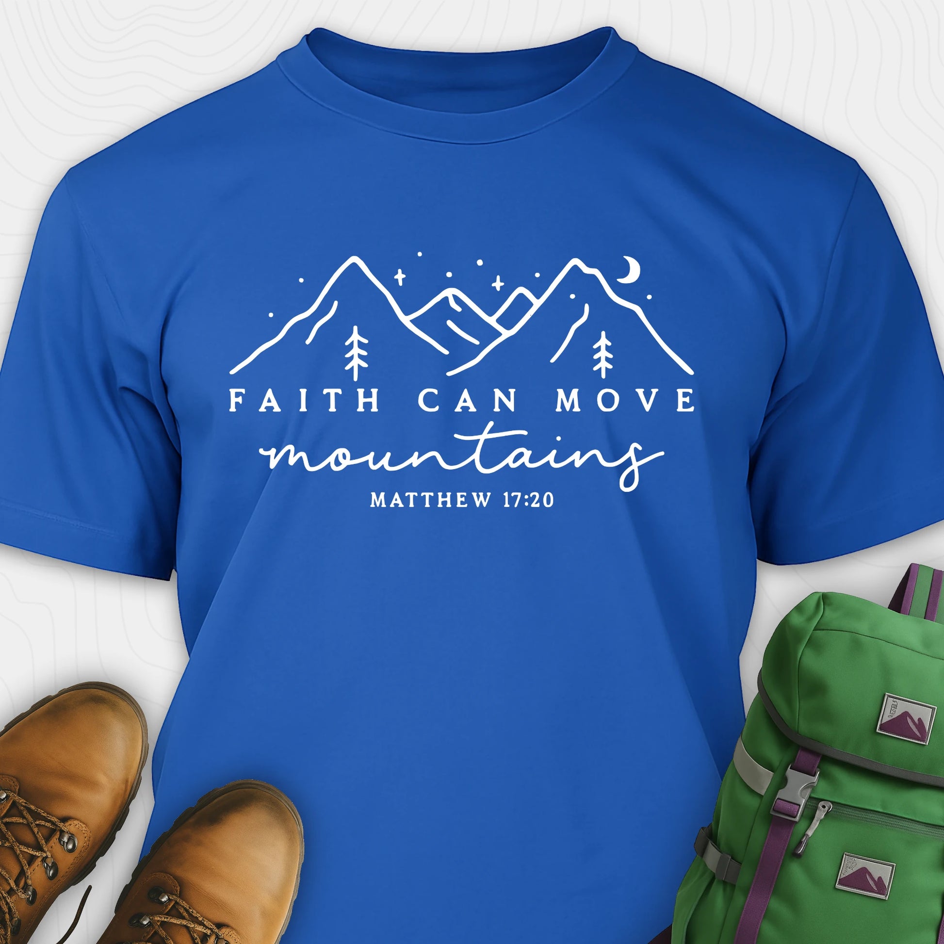 Blue faith can move mountains shirt with mountain scripture design, paired with hiking boots and a green backpack.