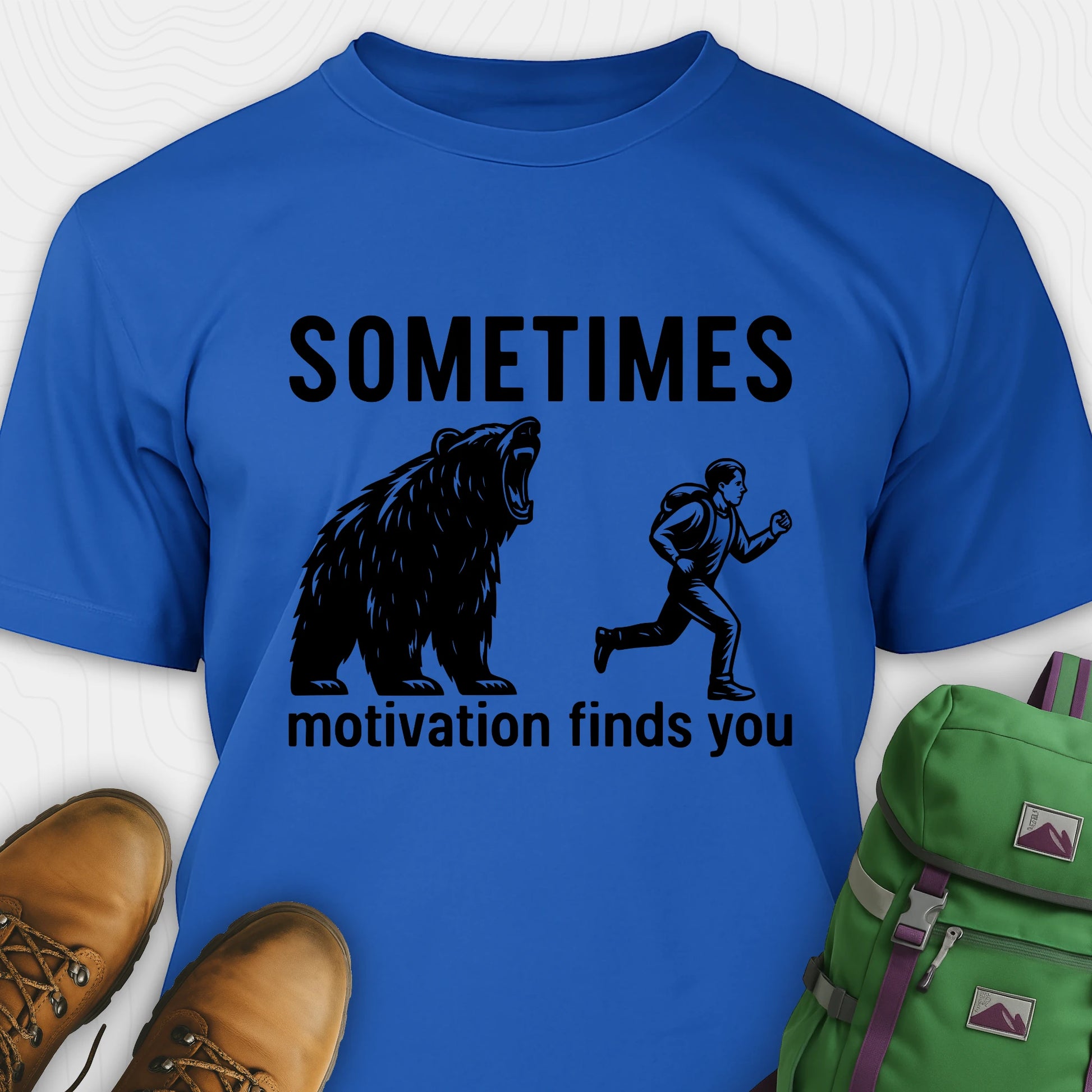 Blue motivational t-shirt with bear and person graphic and text 'SOMETIMES motivation finds you' on a white background.